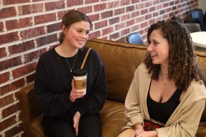 Smiling at her friend, senior Helen Springer sits on the couch at her favorite coffee shop, Summer Moon, Thursday, Jan 12. “I normally go with friends,” Springer said. “I like having people to talk to and I feel a little less awkward.” 