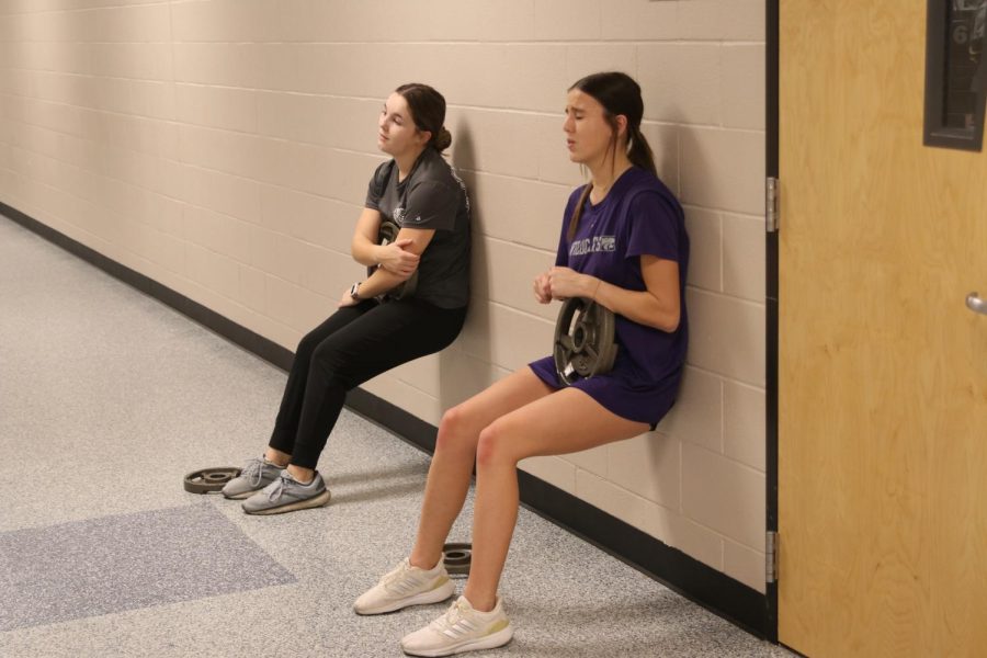Sophomore Molly Griffin and freshman Kinley Ruder wall sit with weight on their legs.