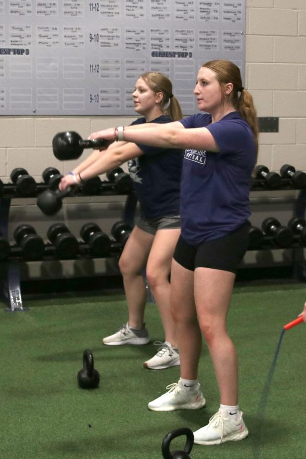 Junior Annabelle Alena and senior Macee Moore swing the kettlebell forward.