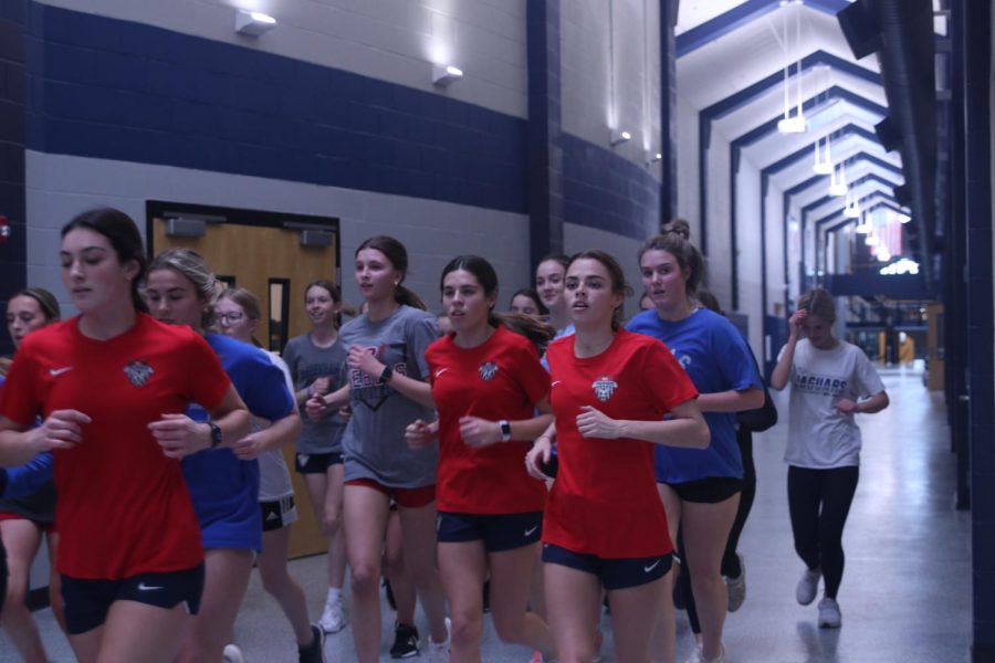 Looking forward, the girls run as a group through the halls.