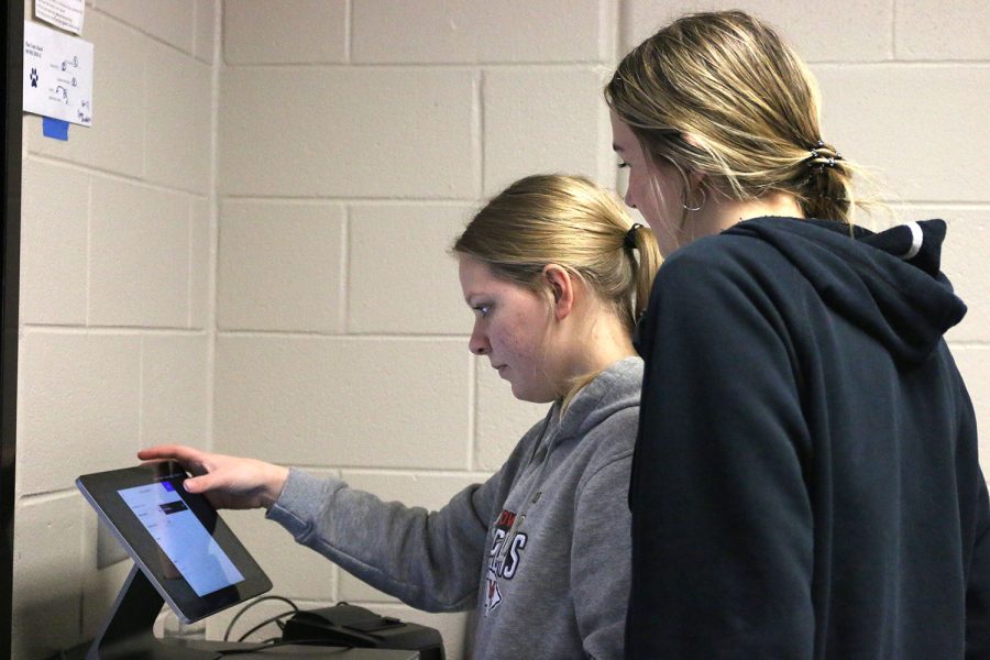 Looking over junior Annabelle Alena’s shoulder, senior Libby Strathman attempts to fix a minor problem with the checkout kiosk.