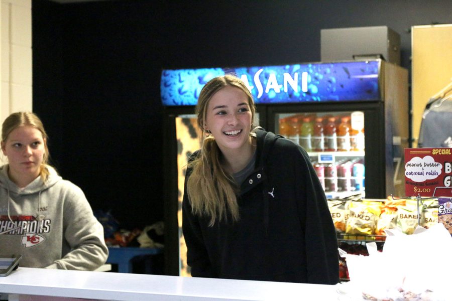 Looking over the counter, senior Libby Strathman beams at the first student-customers in line at the Catty Shack.
