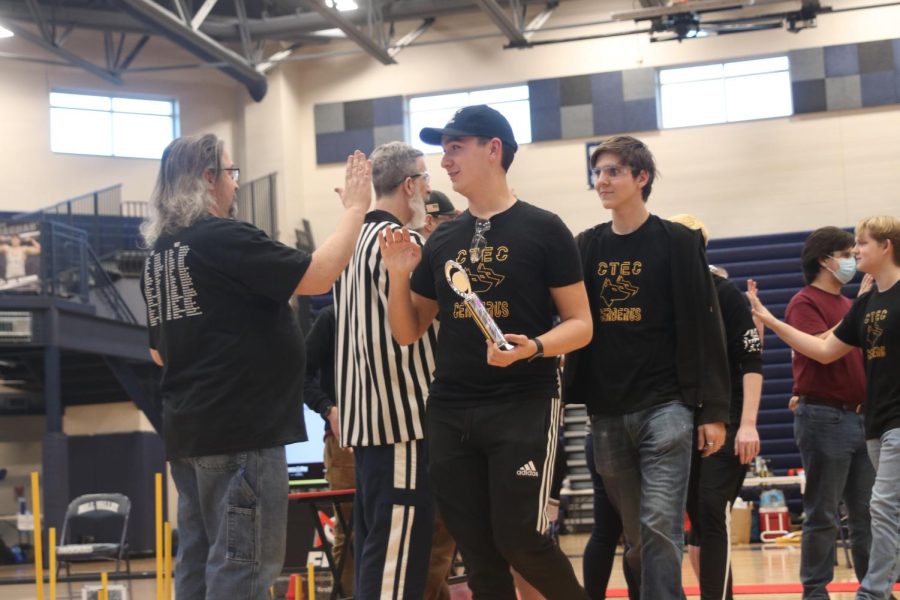 Holding the championship trophy, senior Isaac Steiner high fives the volunteers of the event.