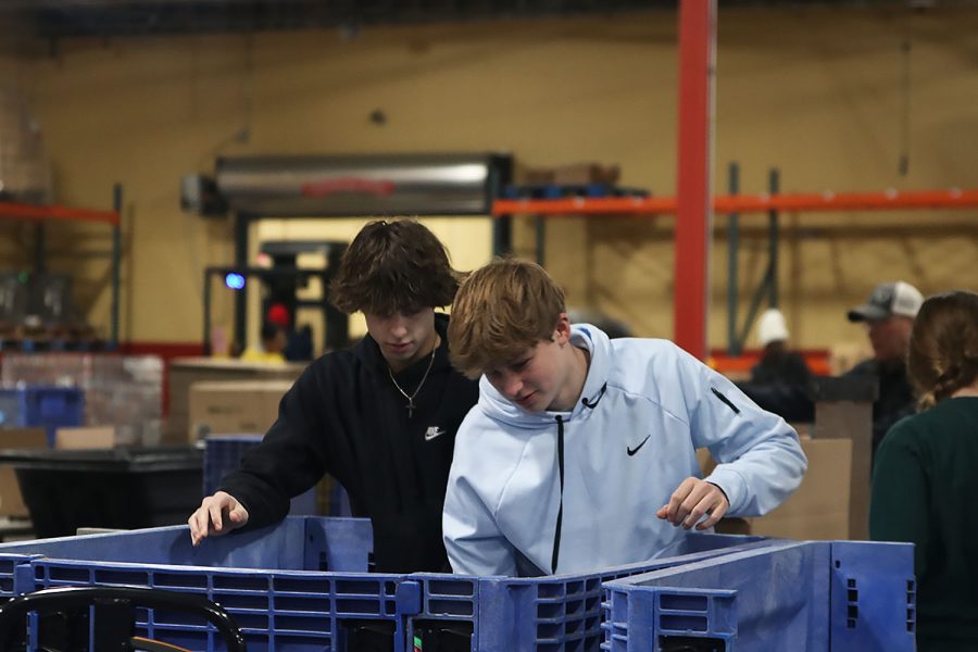 Freshmen Blake Jay and Cannon Fields sort through large blue bins that hold the arrangement of different items. 