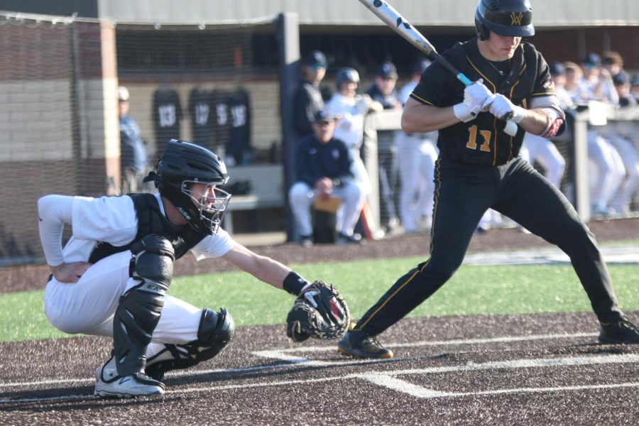 Squatting down, senior Matt Weis catches the ball as the batter attempts to swing.