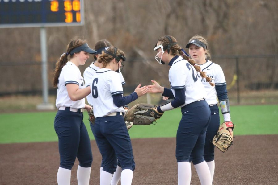 Coming together for a huddle, the girl’s softball team high five each other.