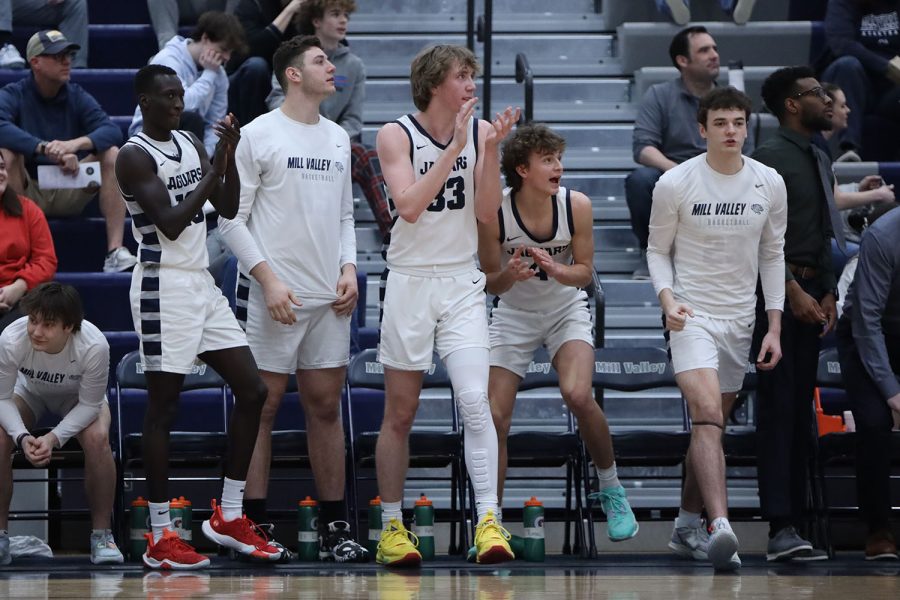 Celebrating their teammates basket, junior Mason Kemp leads his team on the bench in cheering. 