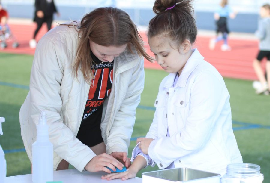 At her tattoo booth, junior Ella Hansen applies temporary tattoos to a girls hand.