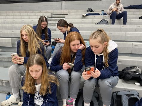 Looking at their phones, girls basketball players wait in the Shawnee Mission East gym between their arrival at the school and warm-ups before their game Friday, Feb. 10. 