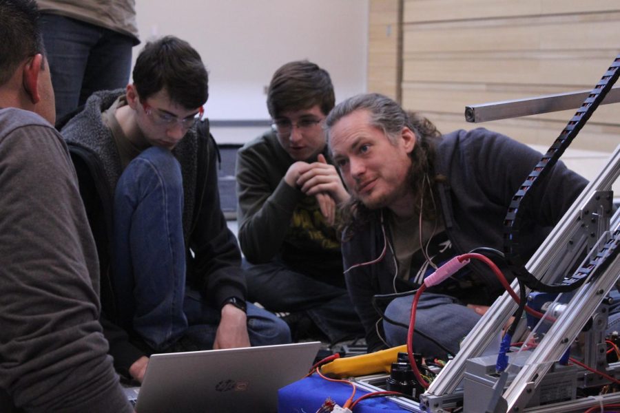 De Soto junior and programming sub-team captain Jack Williamson, junior Sebastian Smith and mentor Neil McLeod examine the varsity teams code to ensure the robot will work during reveal, Saturday, Feb. 25