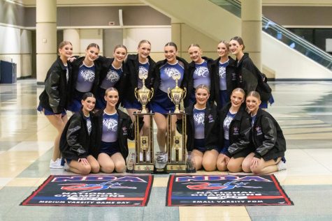 The Silver Stars dance team smiles triumphantly as they pose in front of their two national title awards in the medium varsity game day and small varsity pom divisions.