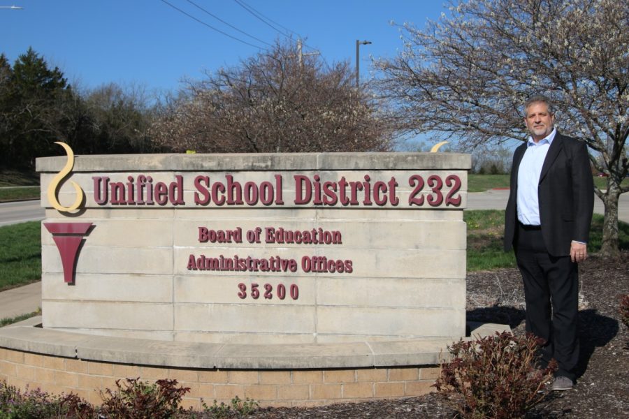 Posing next to the USD 232 sign outside of the central office building, superintendent Dr. Frank Harwood proudly presents himself, Tuesday, April 11. Harwood is to retire from USD 232 June 30 following seven years of district service.