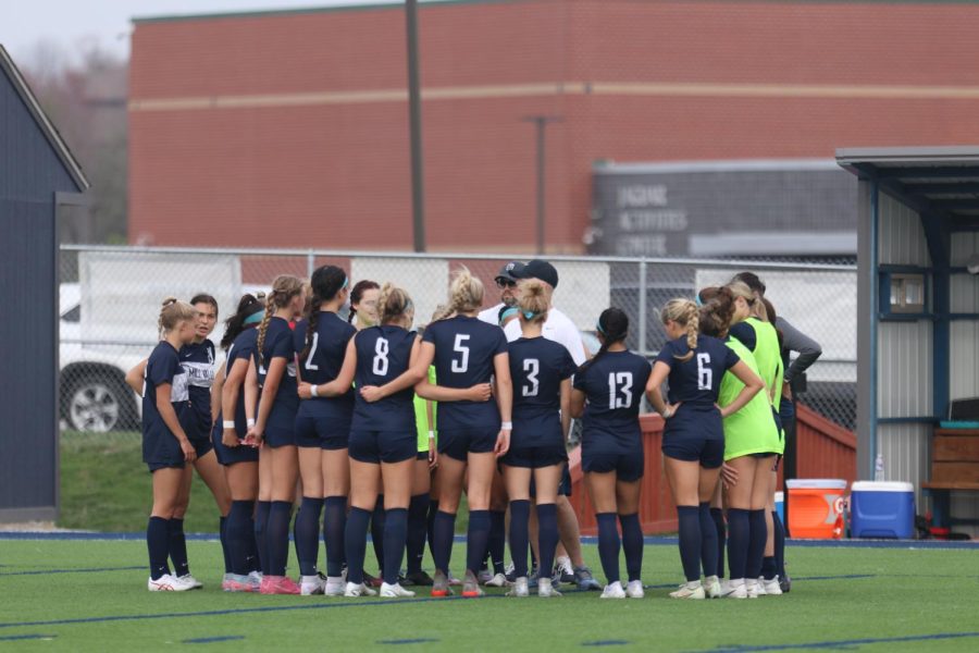 Before their home game against Olathe North, the girls soccer team huddles for a pep talk from head coach Jason Pendleton and assistant coach Justin Crawford.  