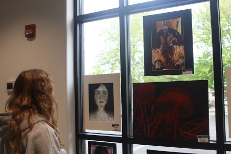 A student observes artwork by senior Kenall Lee and juniors AJ Lauer and Emily Summa at the art show at the Country Club Bank Thursday, May 4.