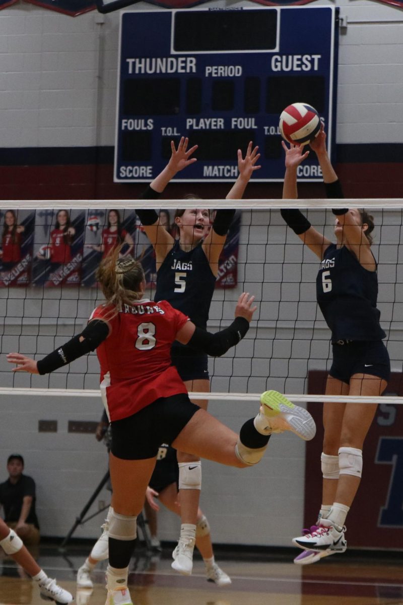 Reaching over the net, junior Saida Jacobs and senior Kaitlyn Burke attempt to block the ball from going over the net. 
