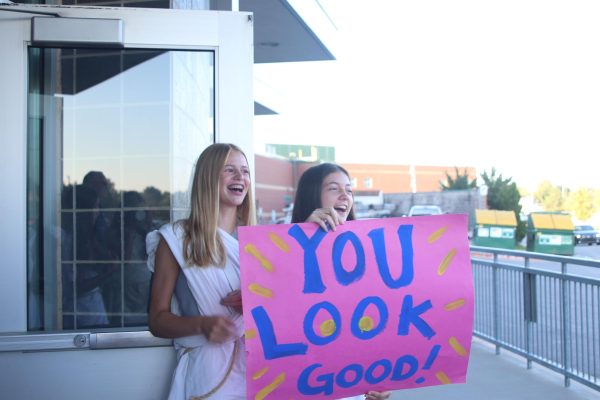 Cheering with their sign, juniors Brooklyn Markovich and Calista Marx welcome the freshmen into the school.