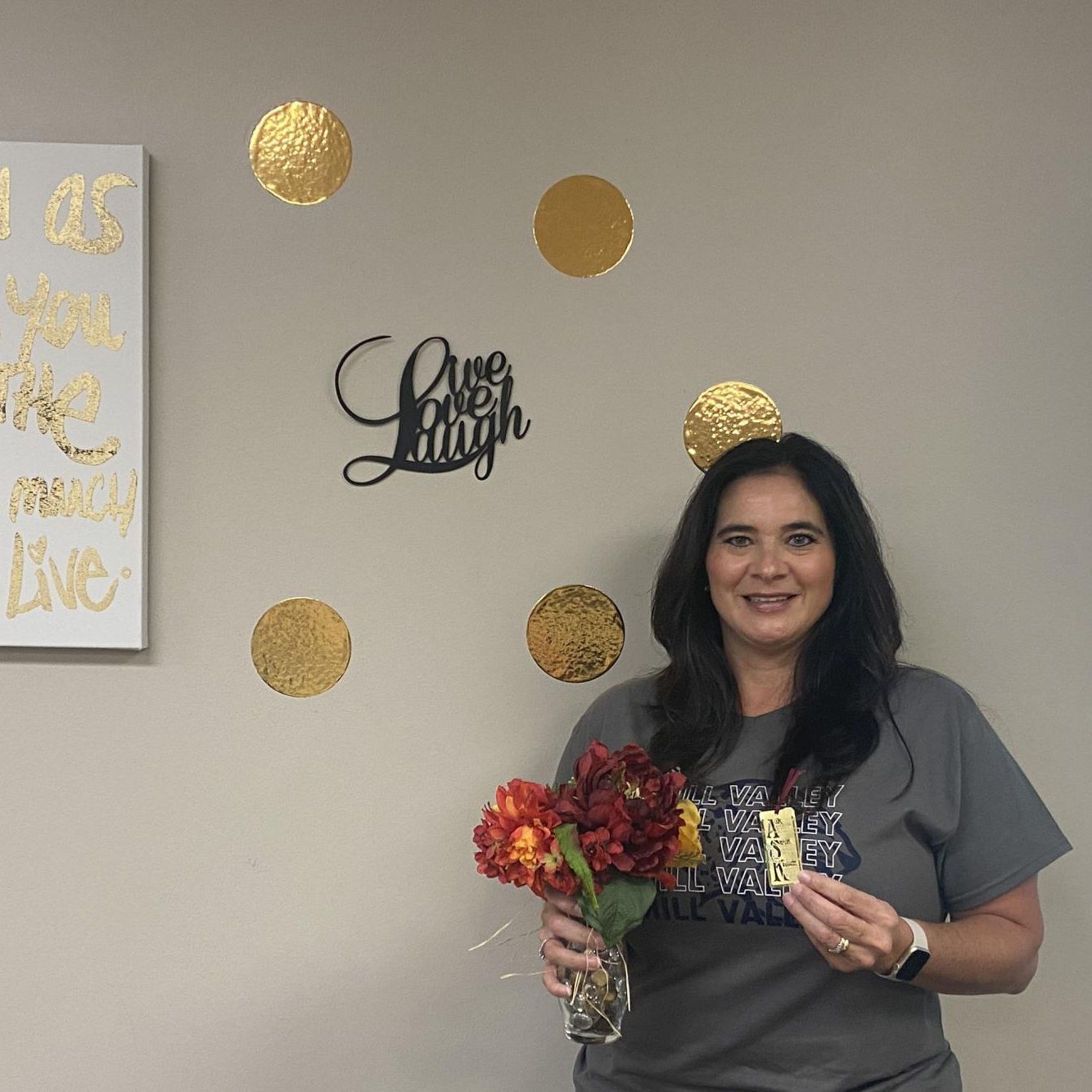 Ms. Swafford holds up two important items to her, flowers and her Ask, seek, knock. Her backdrop is a live, love, laugh sign along with a laugh as much as you breathe, love as much as you live canvas.  These items remind her that [shes] not alone, and [shes] happy.