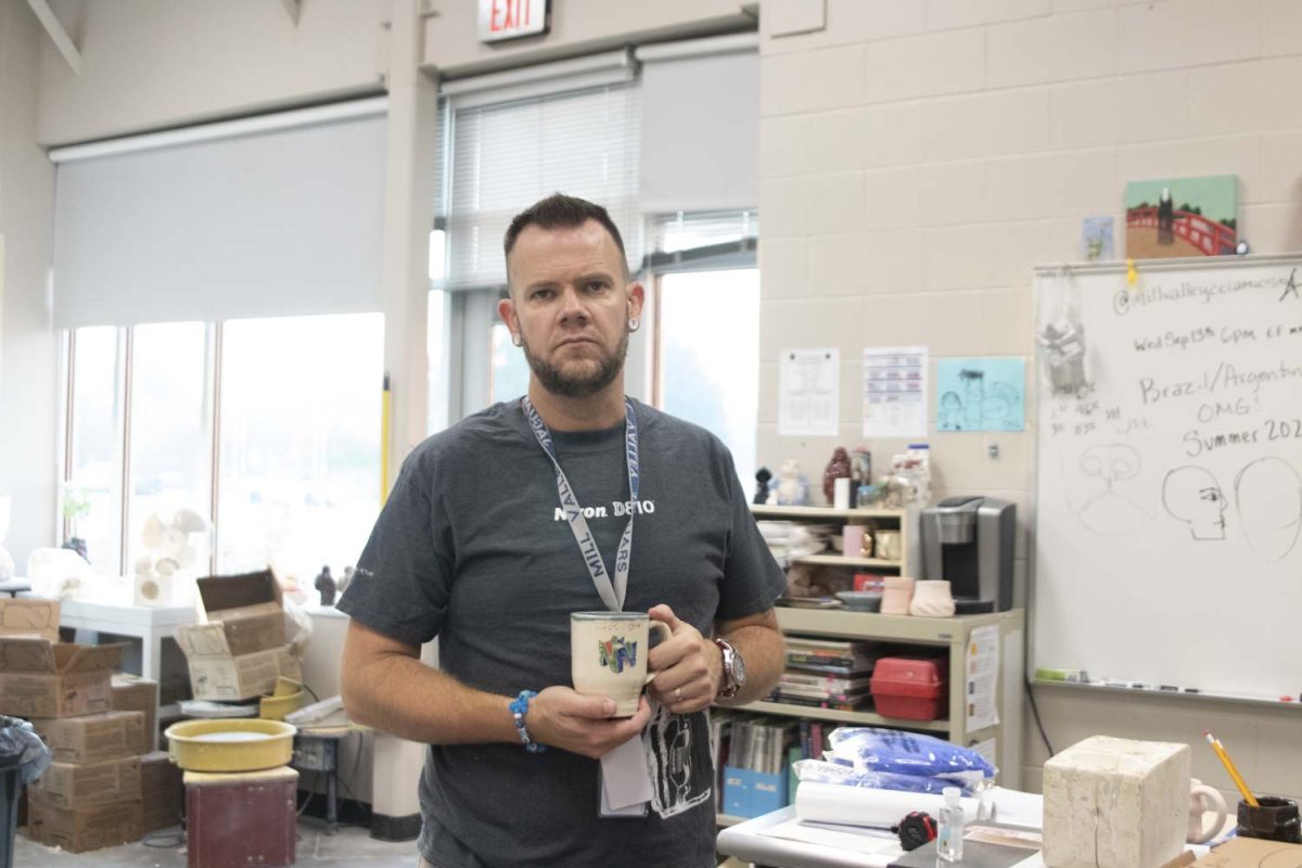 Standing in his classroom, art teacher Bryan Lloyd holds his mug.