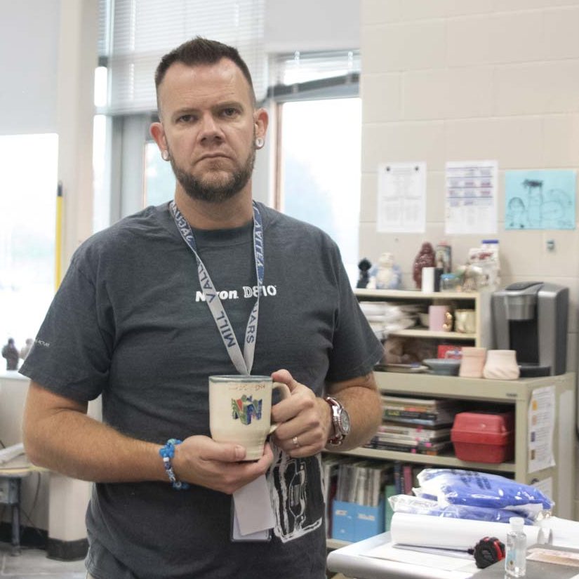 Standing in his classroom, art teacher Bryan Lloyd holds his mug.
