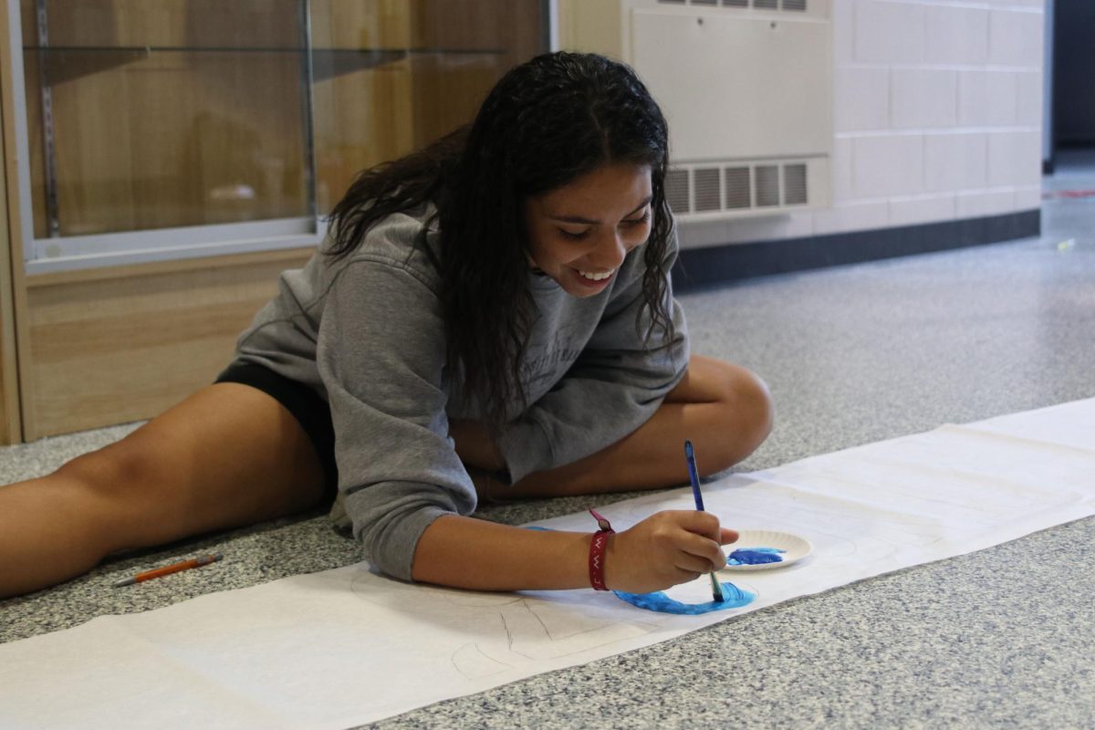 With a smile on her face, junior Kenzie Johnson starts painting a banner for spirit week.