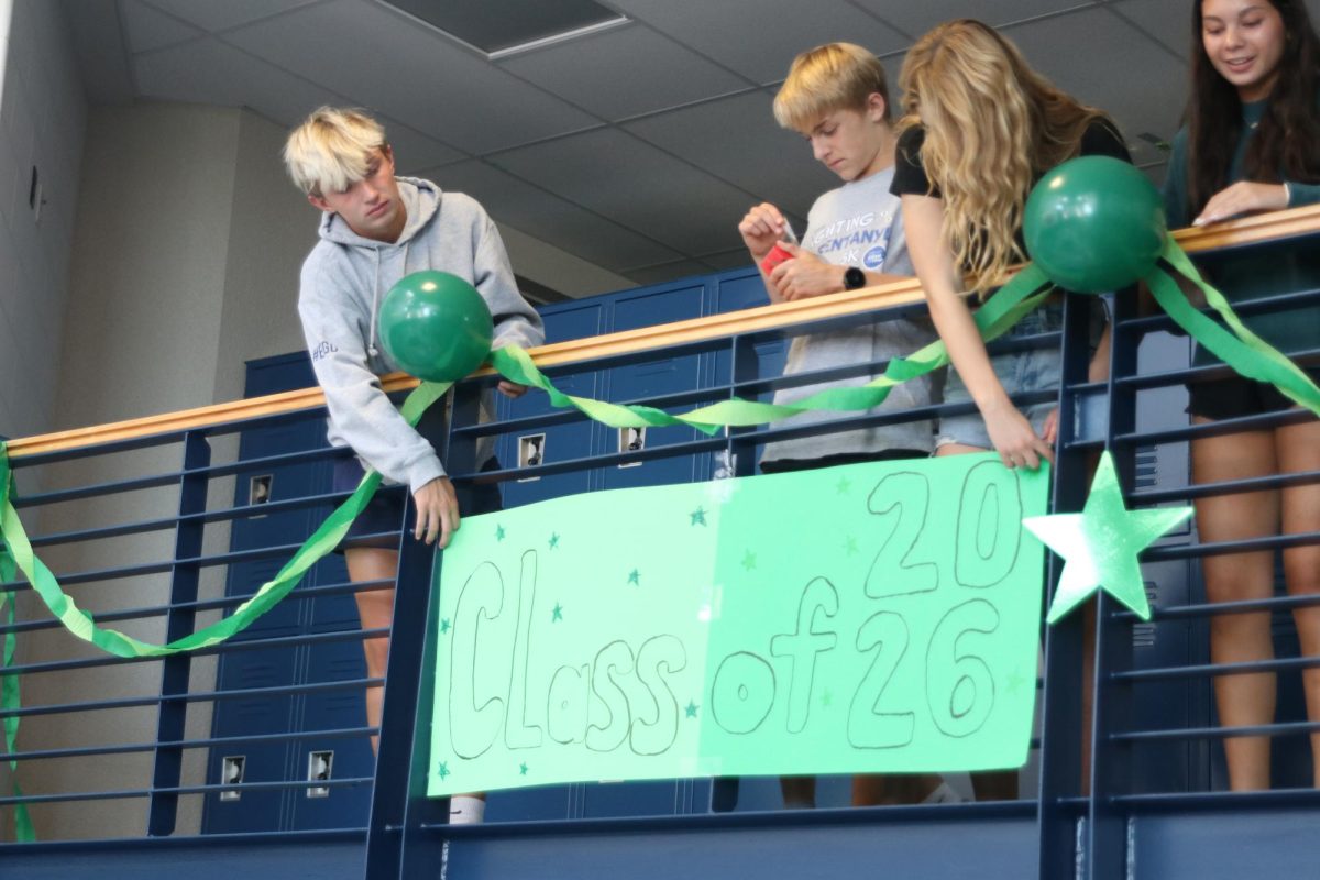 Working together, sophomores Stella Beins and Gus Goetsch hang up a sign in preparation for spirit week.