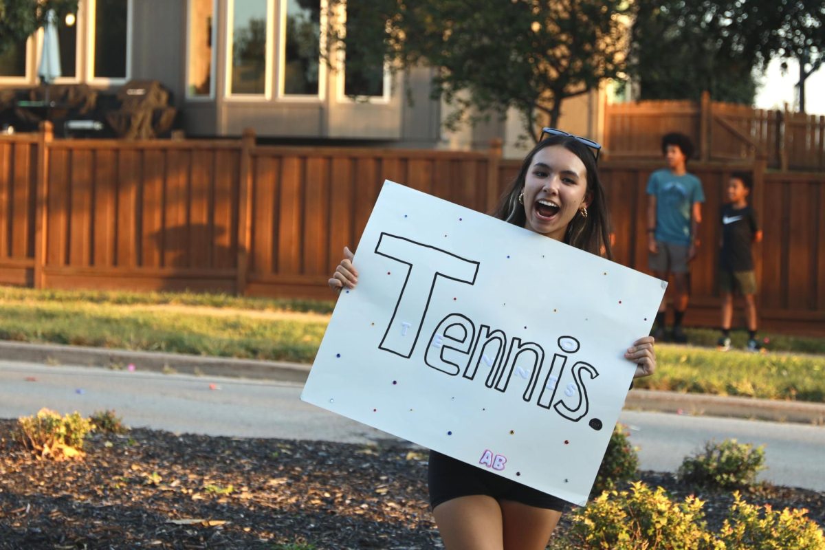 Holding up a sign to promote the tennis team, sophmore Parker Aucoin participates in the homecoming parade.