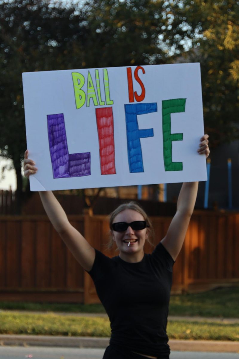 Holding up a sign, sophomore Abby Heinisch participates in the parade as part of the tennis team.