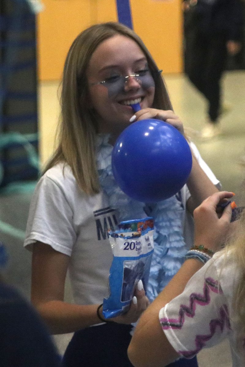 Blowing up a balloon, senior Sam Mullen smiles with her friends.
