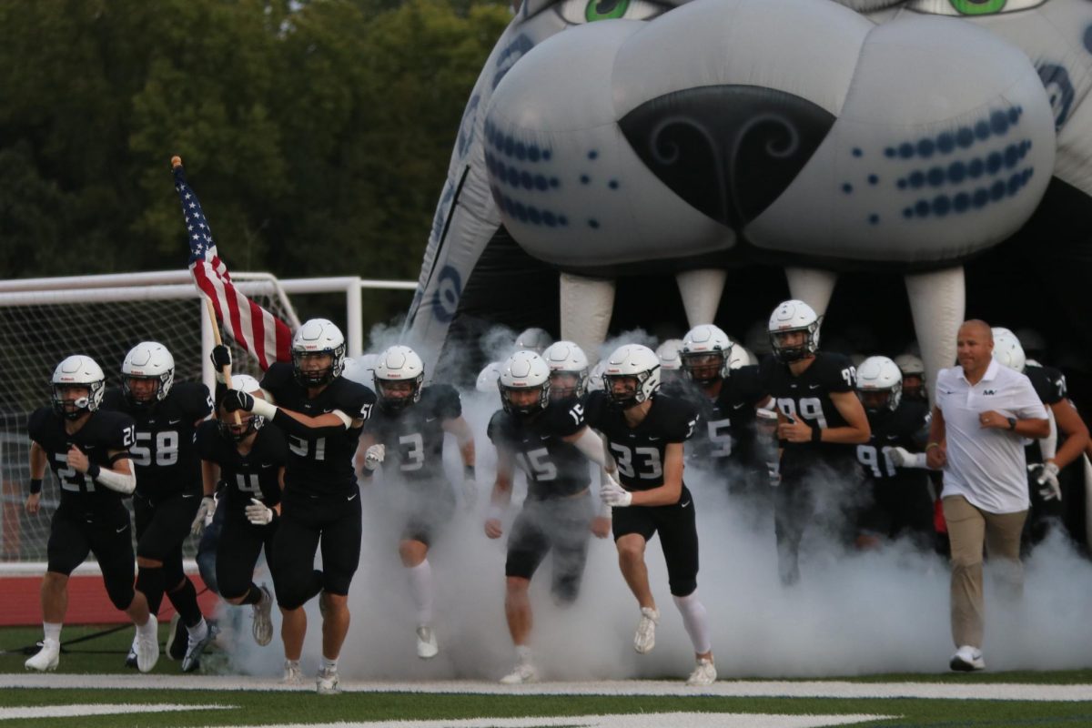 Leading the team onto the field, senior Sam Colletti carries the flag.