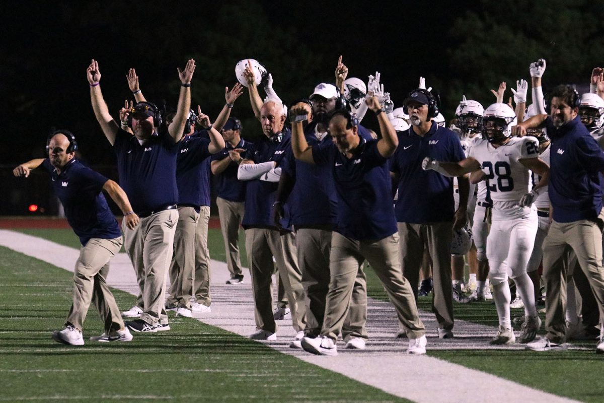 Celebrating a touchdown, the coaching staff walks onto the field with their hands raised. 