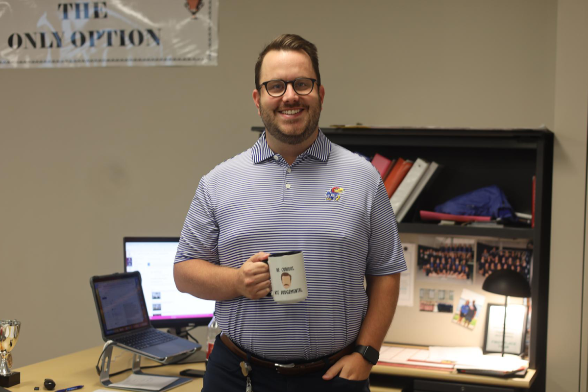 Business teacher Brian Kirkpatrick holds up his Ted Lasso mug that says “be curious, not judgmental,” Friday, Sep. 1. 