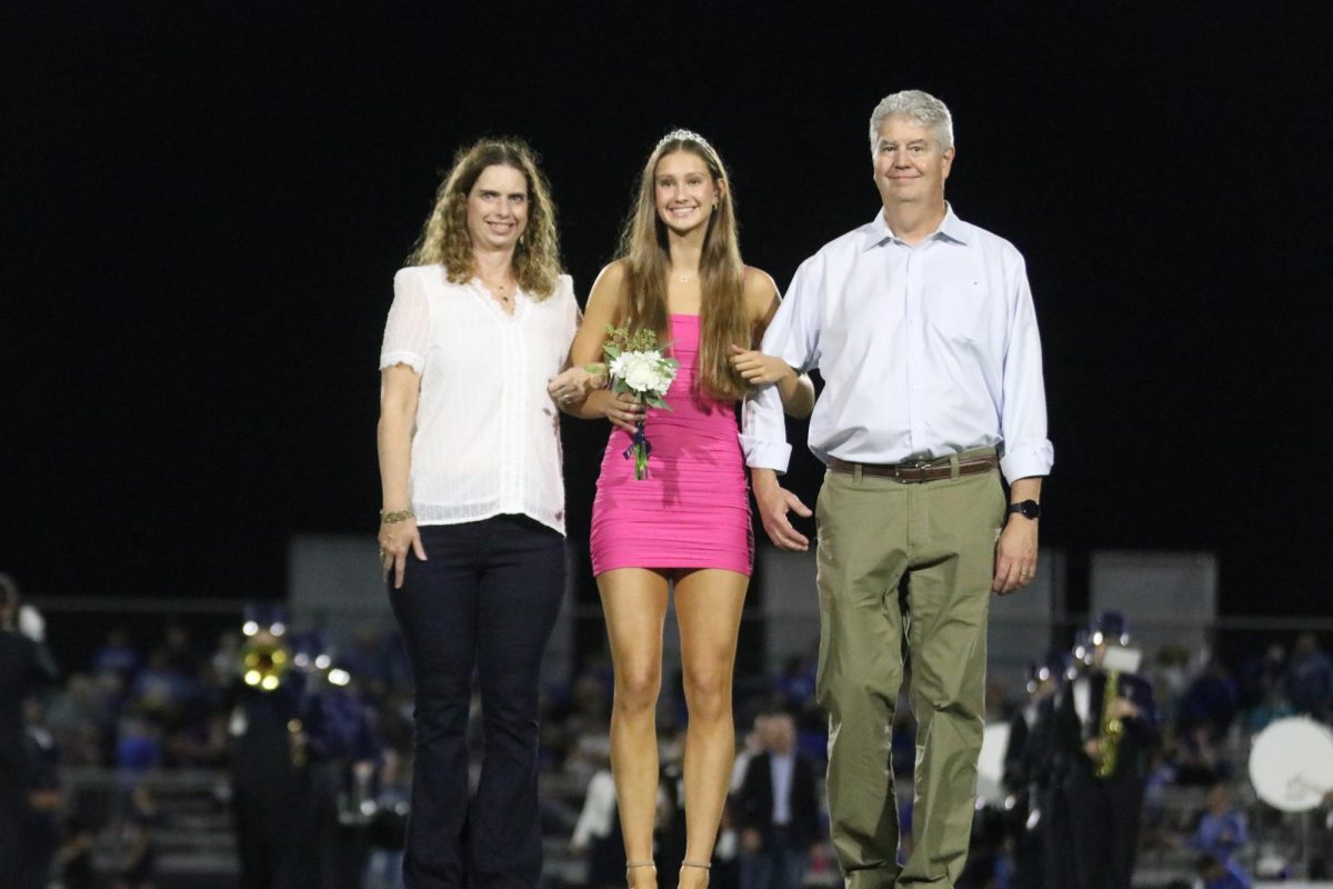 Senior Kaitlyn Burke holds flowers and smiles with her parents 