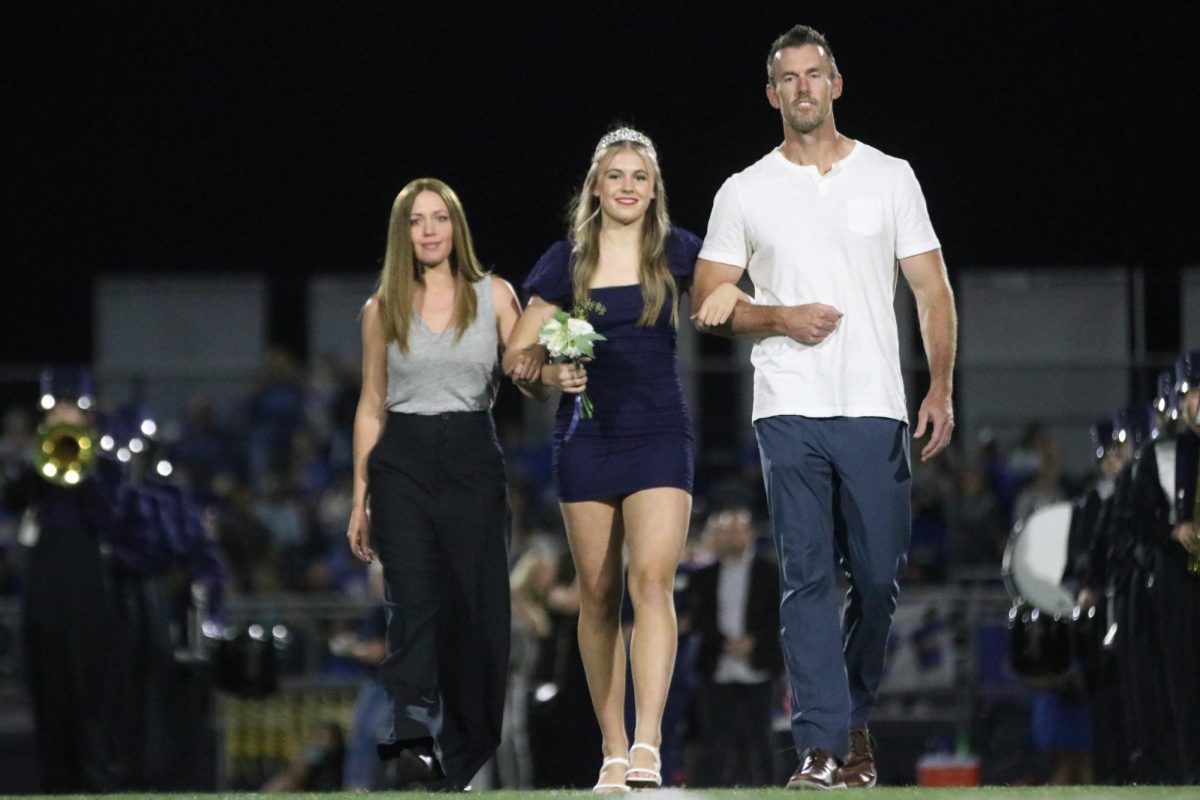 Her arms linked with both her parents senior Halle Wampler walks to her spot after coronation