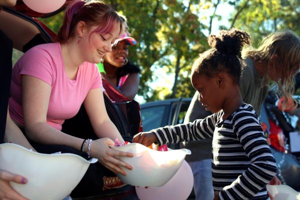 Holding out her bowl of candy to a Kansas City International Academy student, senior Emma Clement smiles. Clement and other members of Youth for Refugees went to KCIA for their annual Trunk-or-Treat Saturday, Oct. 21.