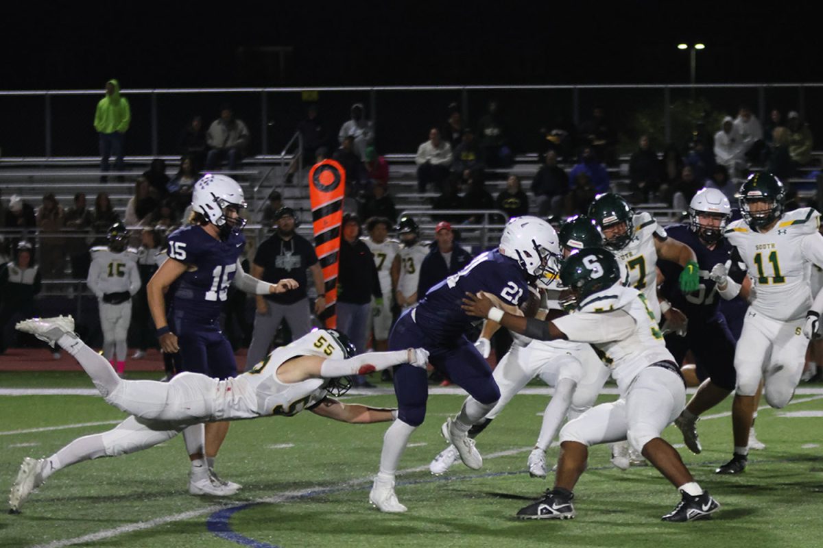 Pushing through the defensive line of Shawnee Mission South, senior Tristan Baker carries the ball to gain significant yards in the third quarter.