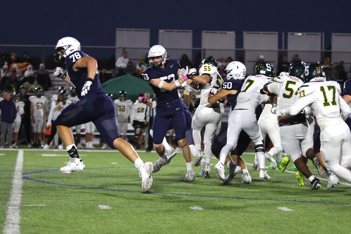 Rushing to prevent Shawnee Mission South defenders from interfering with the play, senior offensive lineman Gus Hawkins sprints away from the starting line.