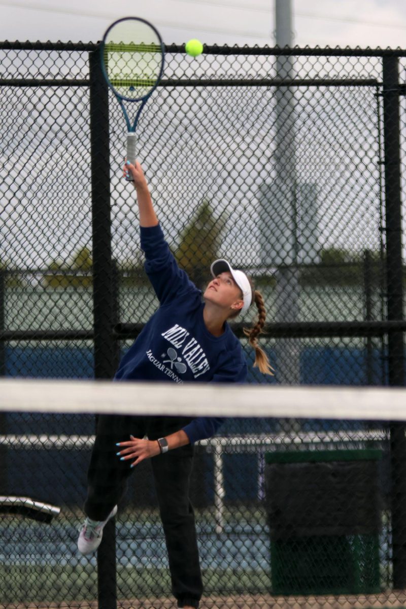 Reaching for the ball, junior Stella Platt sends a serve over the net.