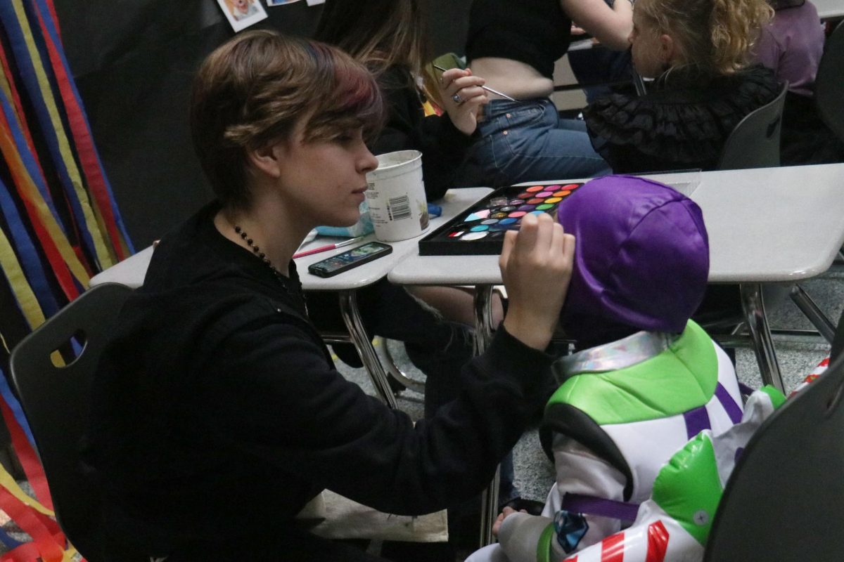 Focused, sophomore Oliver Feiring decorates a child’s face with paint. 