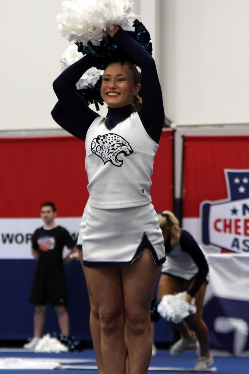 Shaking her pom poms above her head, senior Jaiden Fisher smiles to the crowd.