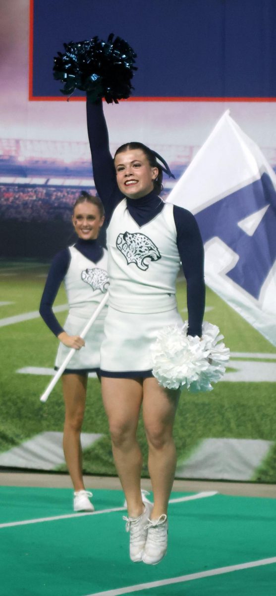 Jumping in the air, sophomore Kyndal Geis shakes her pom above her head.