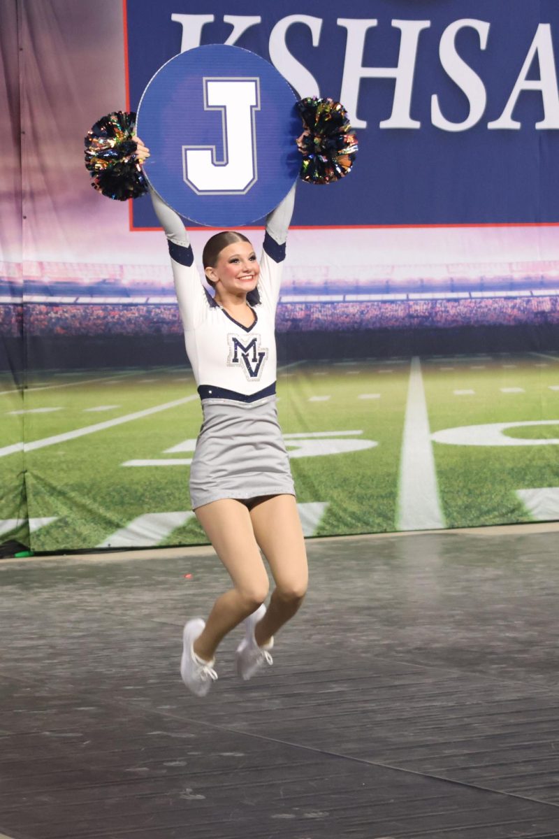 Holding up a sign in the fight song routine, sophomore Ella Jones jumps in the air.