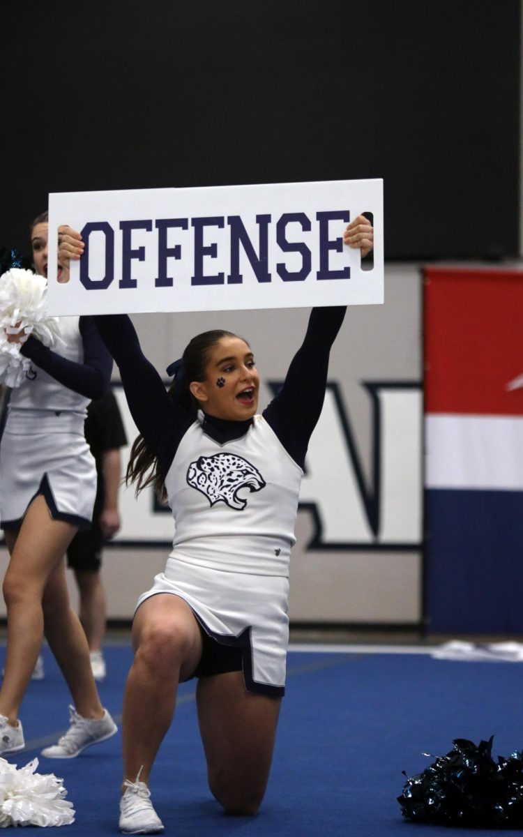 On a knee, senior Makenna Payne holds a sign.