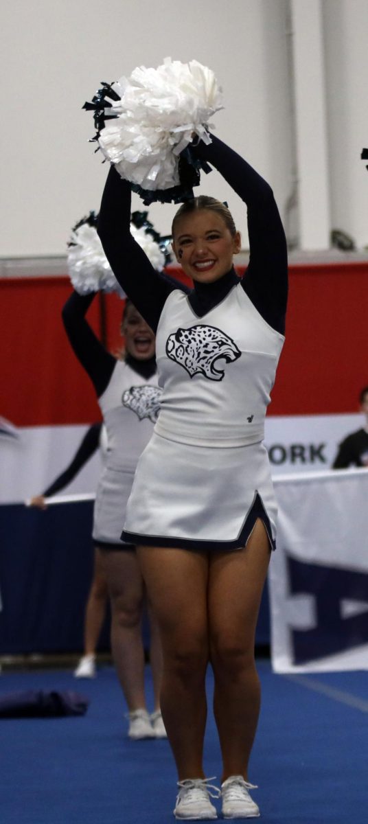 Poms together, senior Maci Burger smiles towards the crowd.
