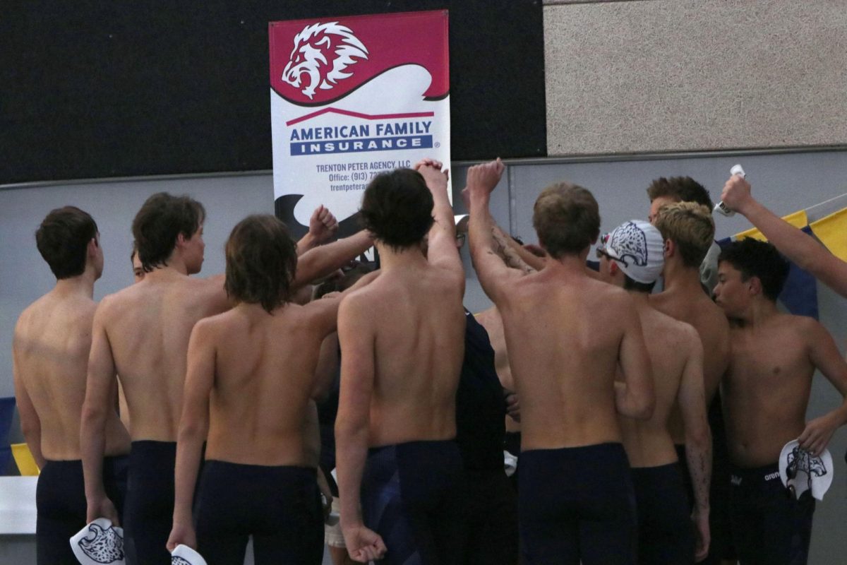 With their arms raised, the boys swim team huddles together before the meet.