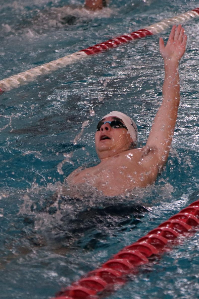 Reaching back, junior Justice Bussell swims backstroke.