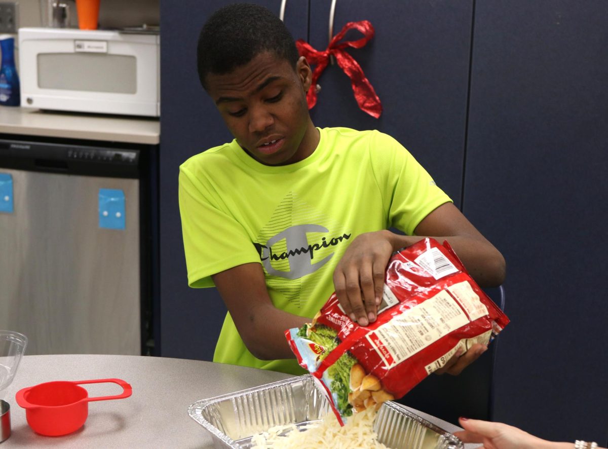 While preparing for their class Christmas party, junior Adairius Newton pours food into a pan. 