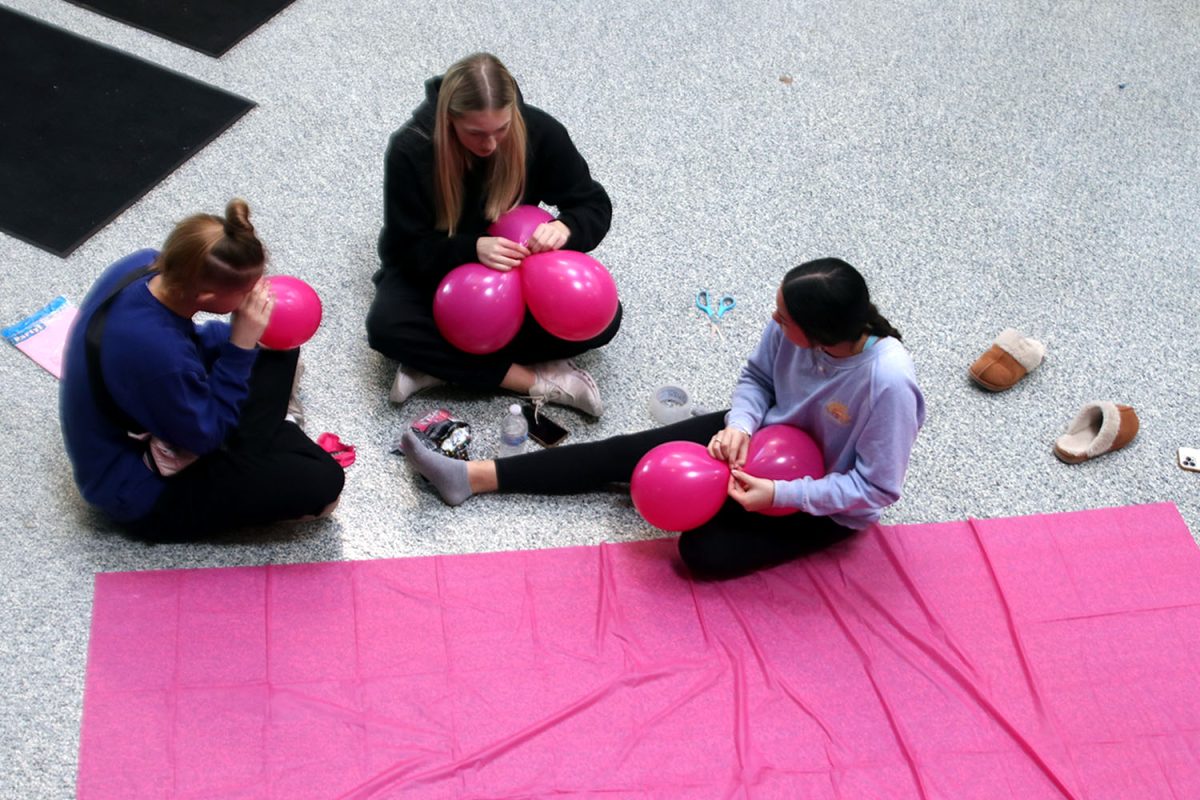Sophomores Sienna Suderman, Callaway Clifton, and Stella Beins tie balloons together for the pink pillars surrounding the Barbie selfie wall.