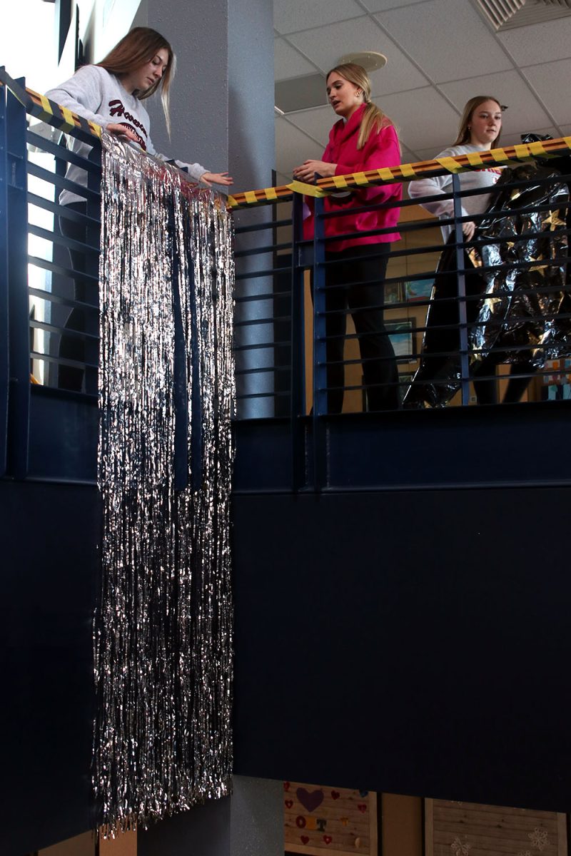 Junior Gracie Kurzejeski and freshmen Reese Miller and Avery Huber hang long tinsel on the central staircase.