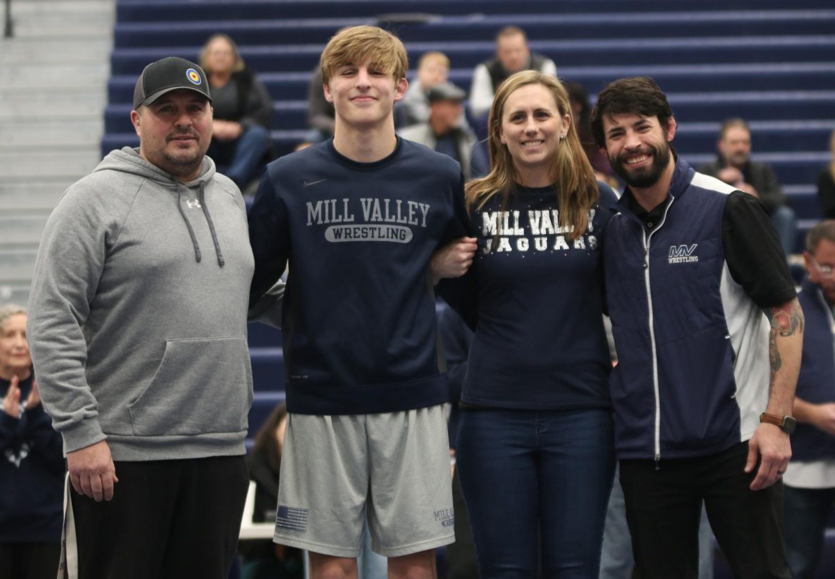 Posing for the camera, senior Colin McAlister stands in front of the camera with his family and head coach Joseph Lazor.
