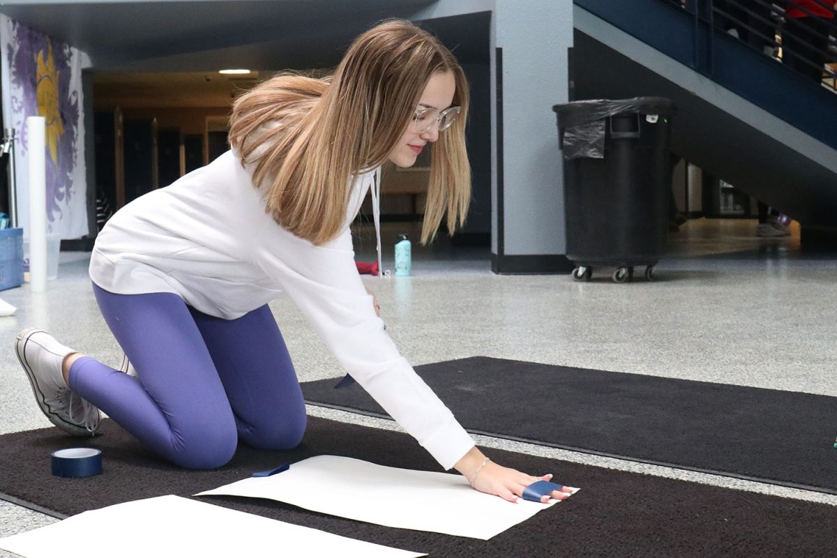 With a smile on her face, sophomore Madi Roberts tapes her poster.
